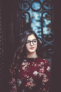 woman wearing black eyeglasses and maroon floral shirt standing in front of black wrought iron gate thumbnail