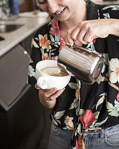 woman pouring coffee from steel pitcher to white ceramic cup making espresso thumbnail