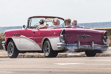 group of men riding on white and pink convertible coupe during daytime thumbnail