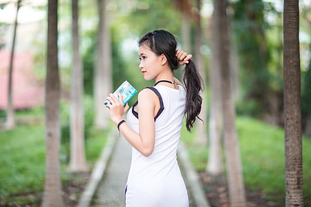 woman wearing white tank top holding hair and looking towards left thumbnail