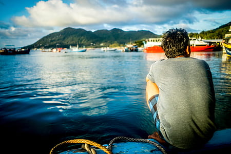 person in gray shirt sitting on blue surface beside body of water thumbnail