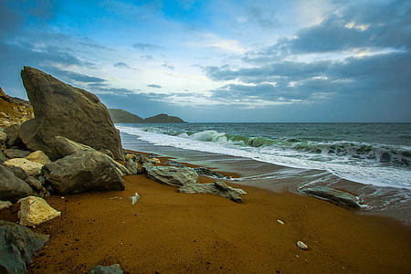 brown boulders on seashore under cloudy sky thumbnail