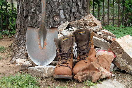 pair of brown boots and black shovel beside some piles of rocks thumbnail