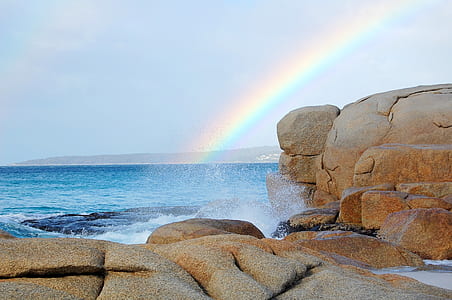 rainbow on body of water near brown rocks thumbnail