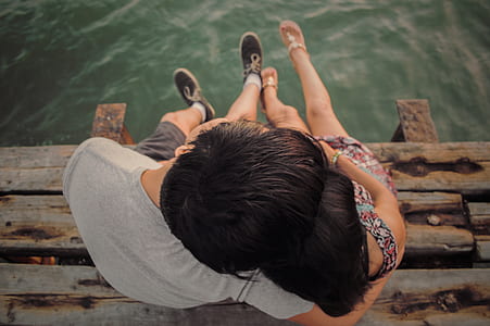 man and woman sitting on wooden dock near near body of water thumbnail