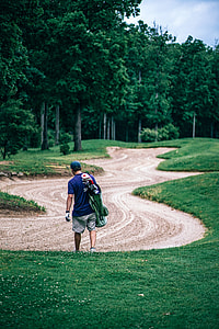 person in blue top walking while carrying golf bag thumbnail