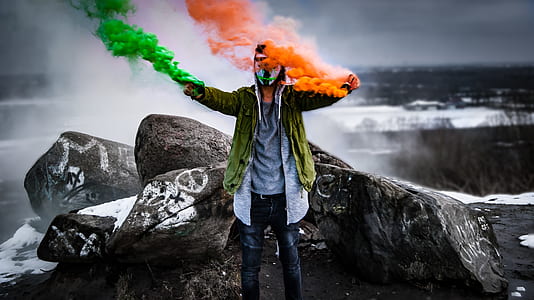 man standing beside rocks holding smoke cans thumbnail