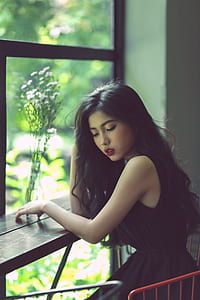 woman in black sleeveless dress sitting near window thumbnail