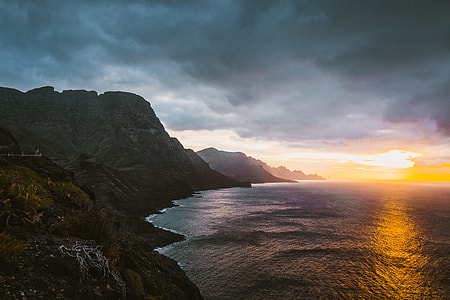 landscape photography of mountain ranges near ocean under cloudy sky during golden hour thumbnail