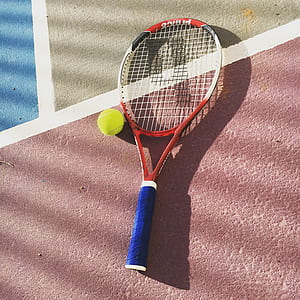red and white tennis racket with green tennis ball on floor thumbnail