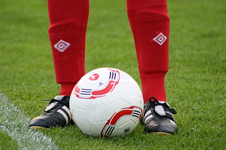 football player standing on green lawn grasses with ball between legs thumbnail