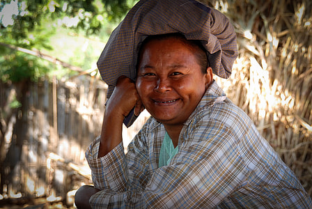 smiling woman in brown and grey plaid shirt with brown textile on head thumbnail