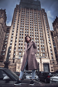 low angle photography of a woman in brown coat in front of building thumbnail