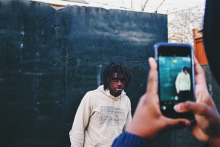 person taking photo of man posing near black painted wall thumbnail
