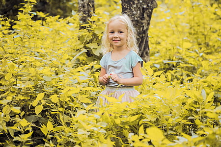 toddler standing beside yellow leaf plants during daytime thumbnail