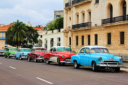 assorted-colored classic cars park on road beside black metal rails thumbnail