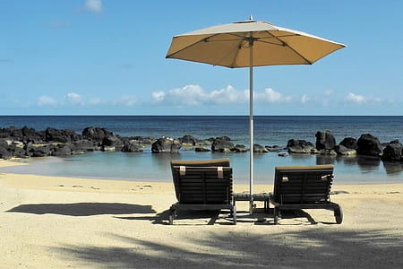 two sun lounger chairs under umbrella by the beach thumbnail