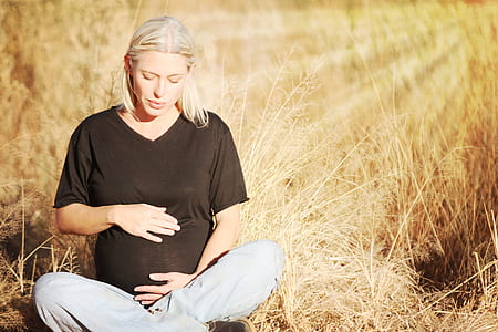 pregnant woman wears black v-neck t-shirt and gray pants seats on brown grass field at daytime thumbnail