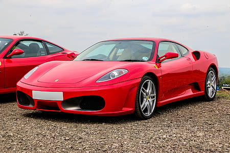 red Ferrari sports coupe beside red coupe at daytime thumbnail