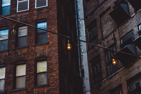 orange light bulbs hanging on a string between brown buildings low-angle photography thumbnail