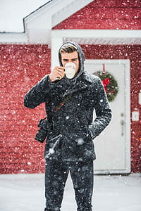 man drinking on cup while standing outside house in snowy weather thumbnail