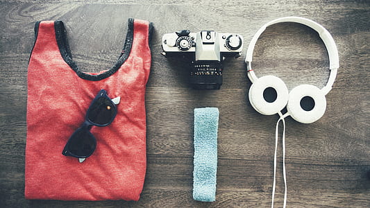 white headphones, black sunglasses, red tank top, headband and camera on brown surface thumbnail