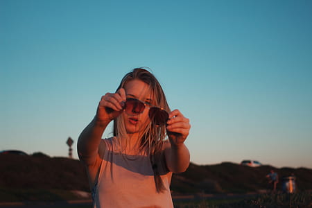 woman standing while holding sunglasses at golden hour thumbnail