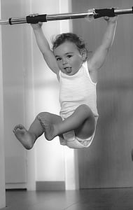 toddler hanging on rod with tongue out grayscale photo thumbnail