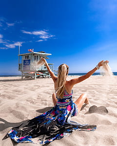 photo of woman sitting on sand near green house during daytime thumbnail