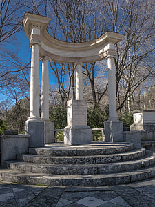 white concrete pillars with a tombstone surrounded by tall trees at daytime thumbnail