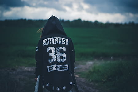 person in black and white hooded jacket near green grasses during daytime shallow focus photography thumbnail