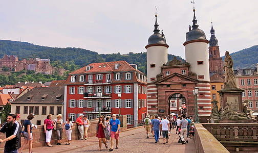 group of people walks on concrete bridge near statue and buildings thumbnail