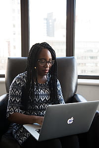 Woman in Black and White Blouse Sitting on Black Leather Chair Holding Her Laptop thumbnail