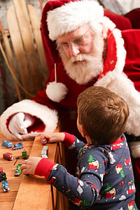 man wearing Santa Claus costume beside boy playing Thomas The Train toys on brown wooden table thumbnail
