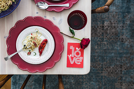 Fancy dinner with seafood pasta, crayfish and red wine by the table decorated with roses thumbnail