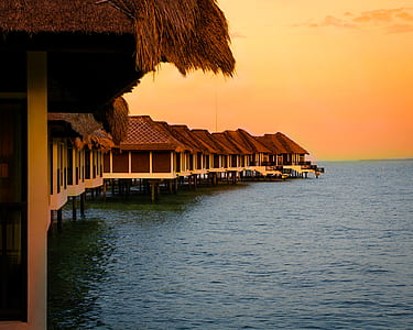 Architectural Photography of Brown Stilt Houses on Top of Sea Under Orange Sky thumbnail