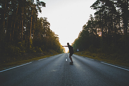 man standing in the road with skateboard during day time thumbnail
