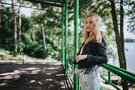 Blonde woman in a black jacket and ripped jeans by a green handrail thumbnail