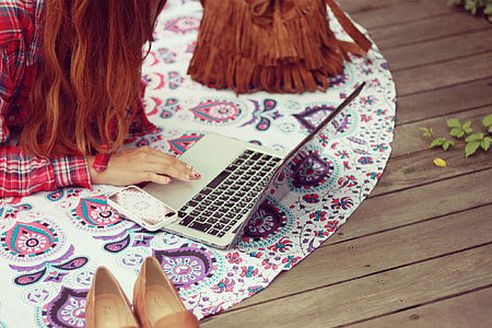 woman holding laptop computer on white and pink floor mat near fringe bag and shoes thumbnail