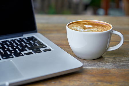 brown and white coffee in white ceramic mug beside of gray laptop computer thumbnail