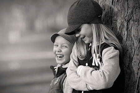 girl and boy leaning on tree trunk grayscale photo thumbnail