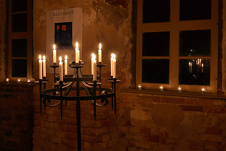photo of round metal candle holder with lighted candles near white wooden framed clear glass window in dark room thumbnail