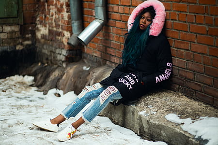 Woman Wearing Black and Pink Parka Leaning on Brown Brick Wall thumbnail