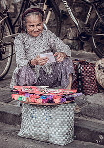 woman sitting on grey concrete pavement selling hand fans thumbnail