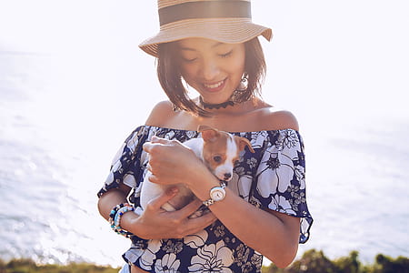 women's blue and white floral off-shoulder shirt holding hogging puppy near sea at daytime thumbnail