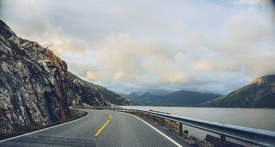 curved road between body of water and mountains thumbnail