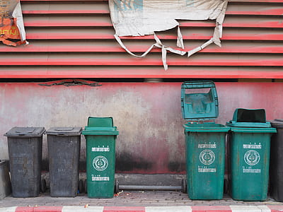 green and black plastic trash bin near red wall thumbnail