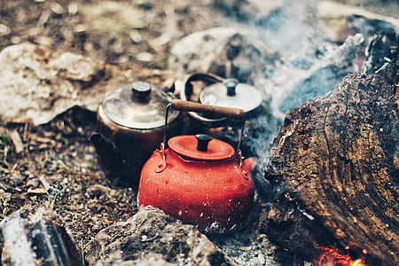 three assorted-color metal kettles in fire near stones during daytime thumbnail
