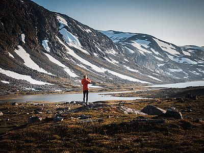 person standing on grass near body of water and snowcapped mountain thumbnail