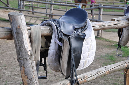 black leather horse saddle hanging on brown wooden fence thumbnail